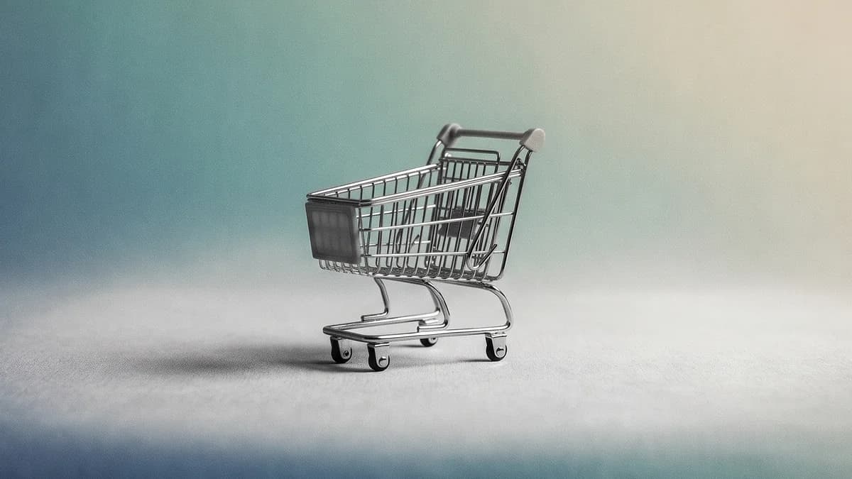 Carrito de supermercado de metal en miniatura y vacío, centrado, en blanco y negro sobre un fondo degradado azul, verde azulado y crema